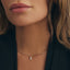 A close-up of a model wearing a delicate gold chain necklace with a small clear teardrop gemstone pendant, styled with a black blazer.