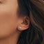 A close-up of a woman's ear wearing a Gold and diamond stud earring with a marquis shape design, set against her brown hair.